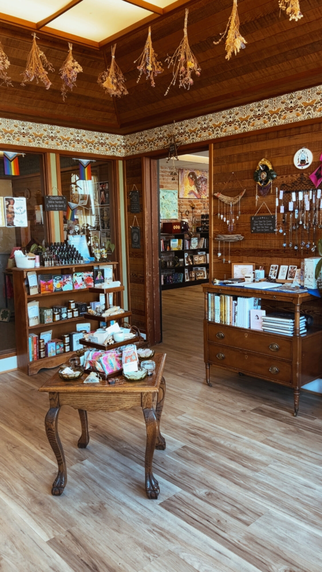 Interior of a cozy shop with wooden furniture, shelves filled with books and items, and a doorway leading to another room.