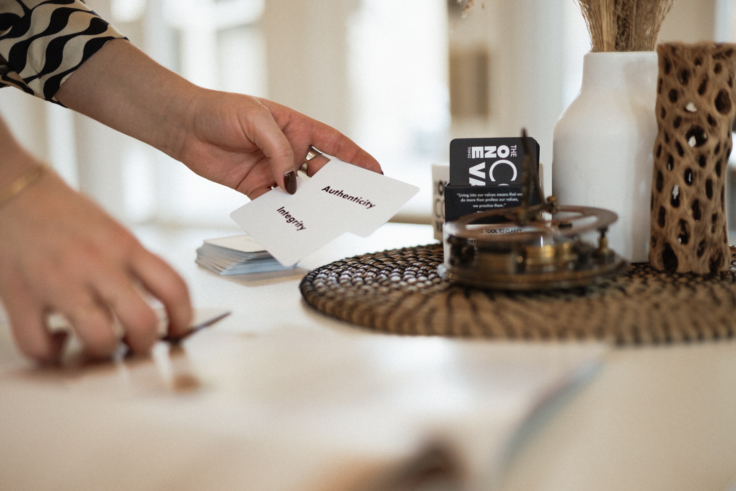 Person's hand holding a small stack of cards or papers on a table with decorative objects nearby.