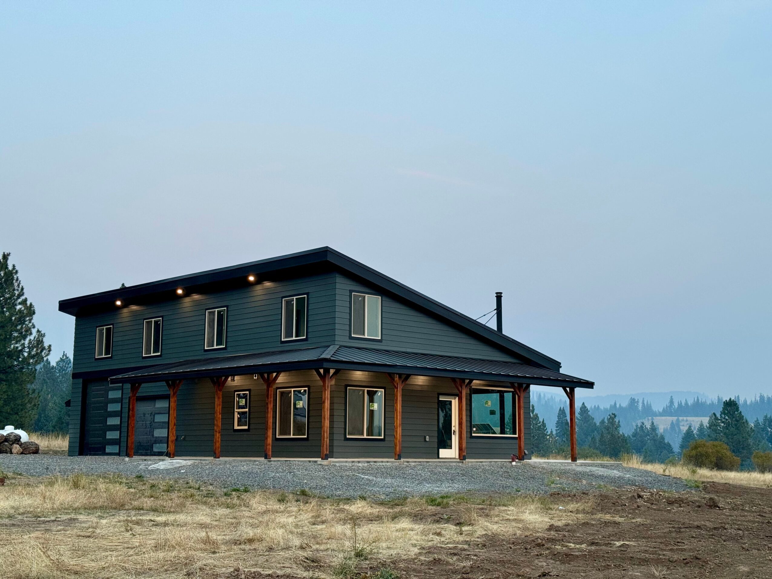 Two-story house with dark blue upper and brown lower sections, large windows, and a covered porch, set against a landscape background.