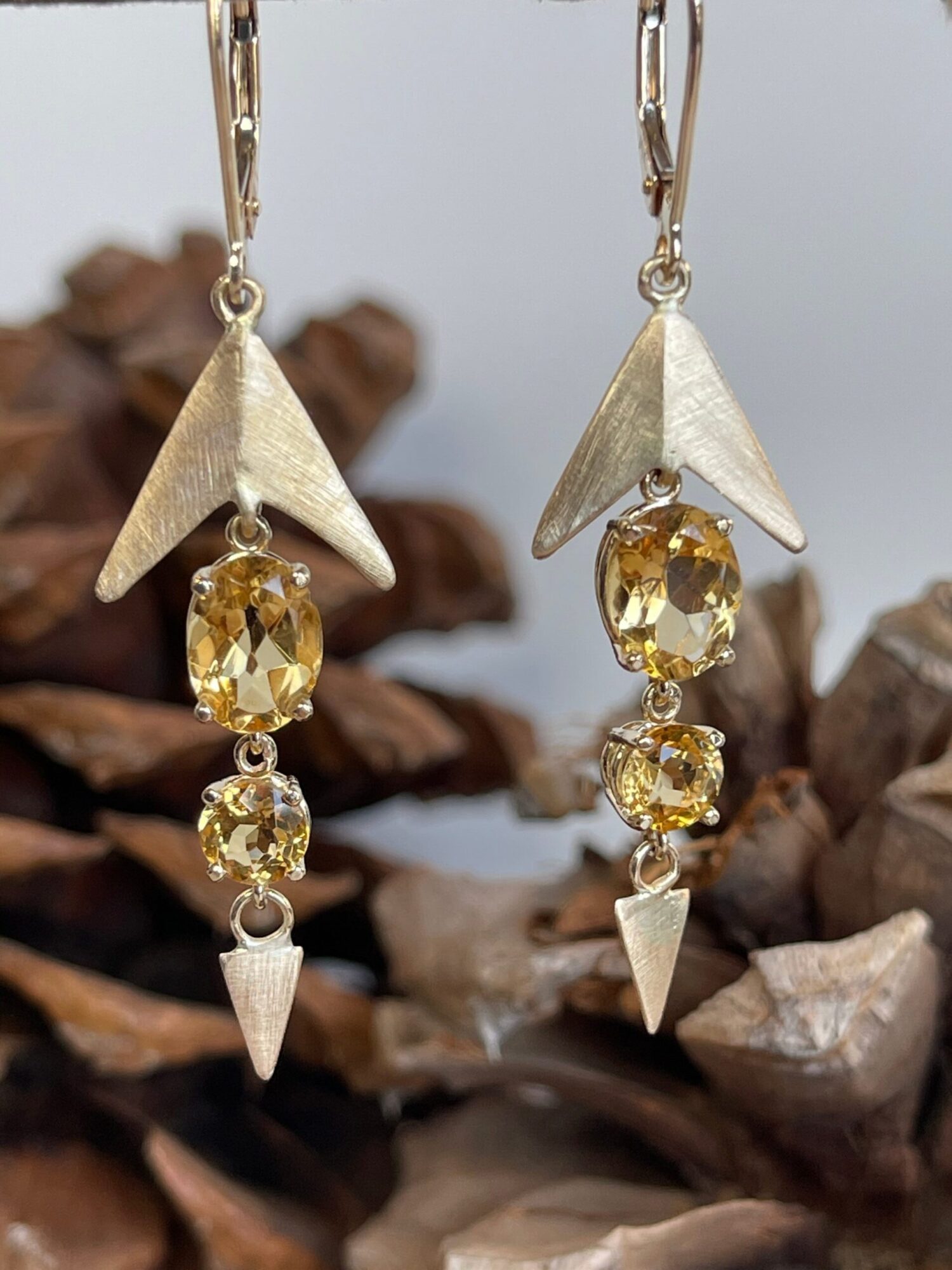 Close-up of a gold and silver earring with yellow gemstones and geometric shapes, against a textured background.