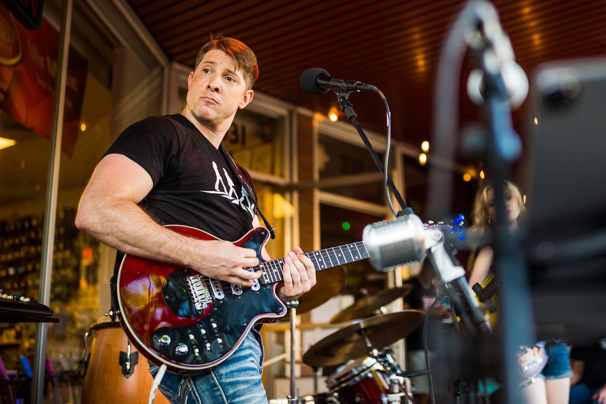 Man playing an electric guitar in a room with large windows and warm lighting.