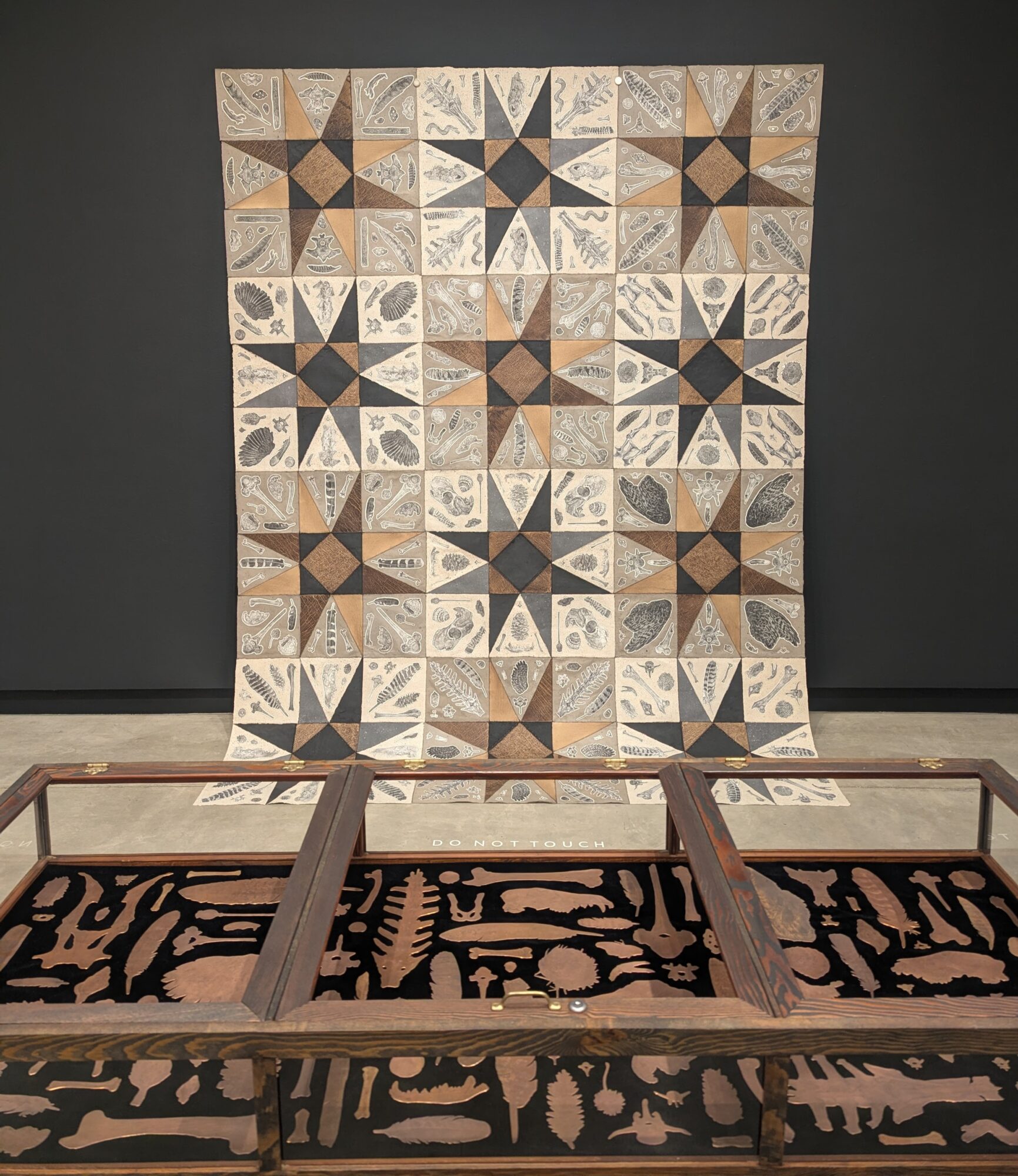 Quilt with geometric star patterns hanging on a dark wall, partially covering a wooden frame and a patterned rug.