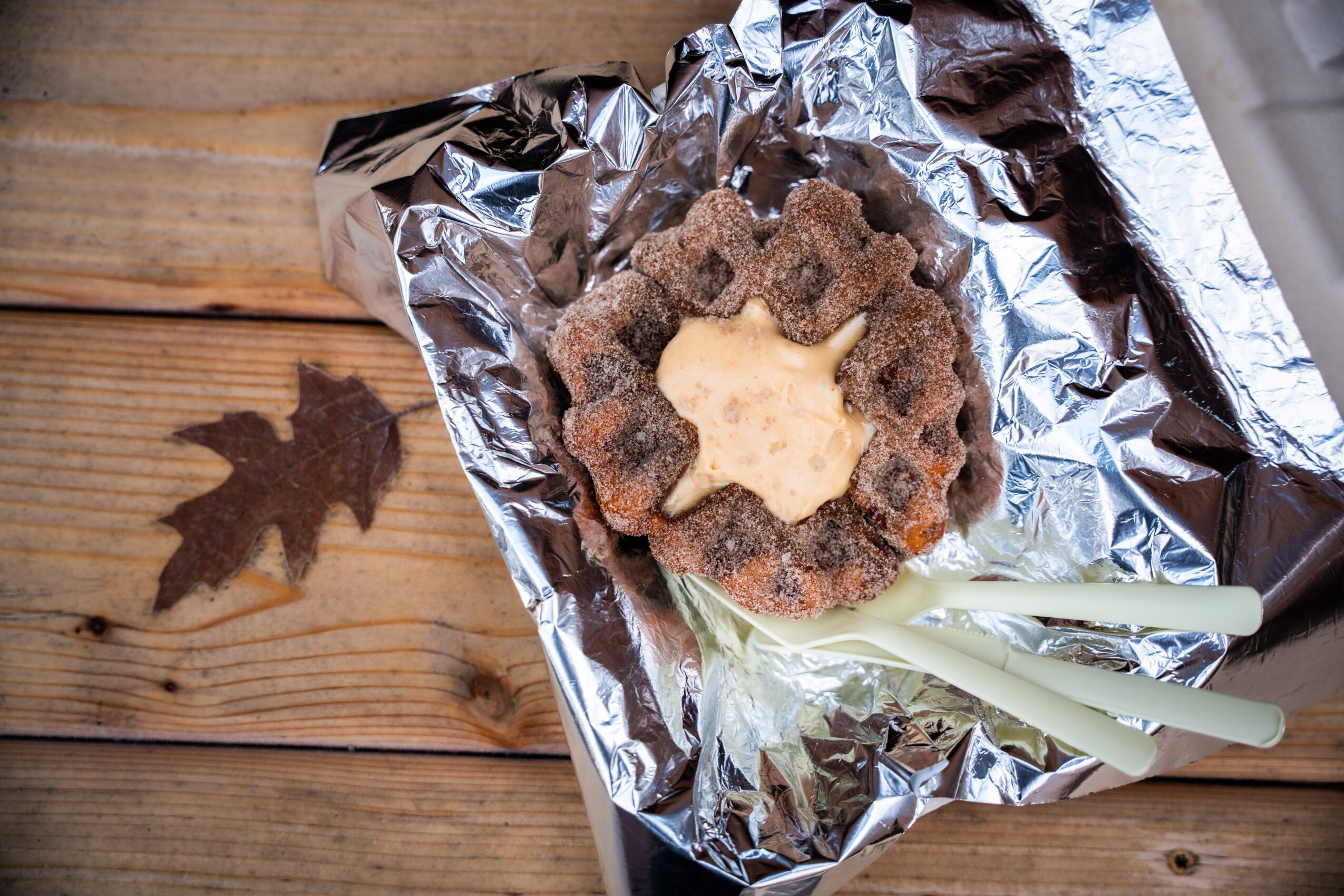 A cookie with a star-shaped center on aluminum foil, placed on a wooden surface with a leaf shadow nearby.