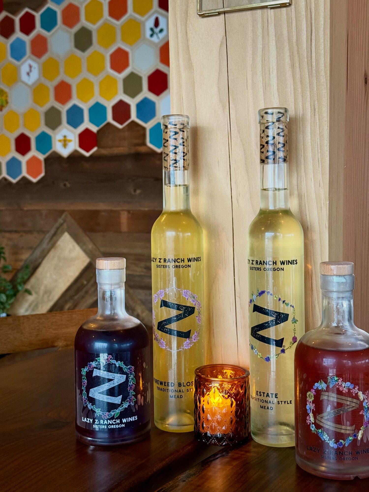 Two tall bottles with yellow liquid, two shorter bottles with dark and red liquids, a small candle, and a wooden background.