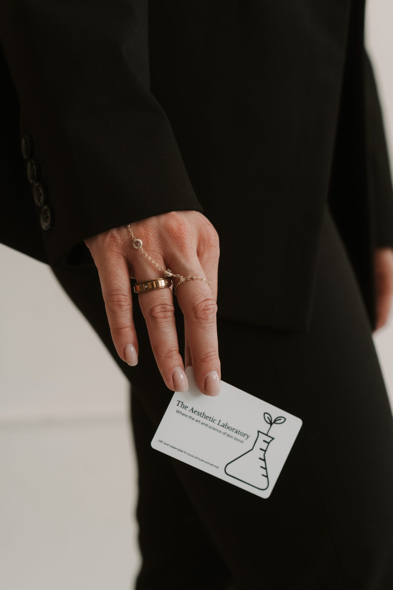 Person in black suit holding a card with a Christmas stocking illustration, fingers with rings, background blurred