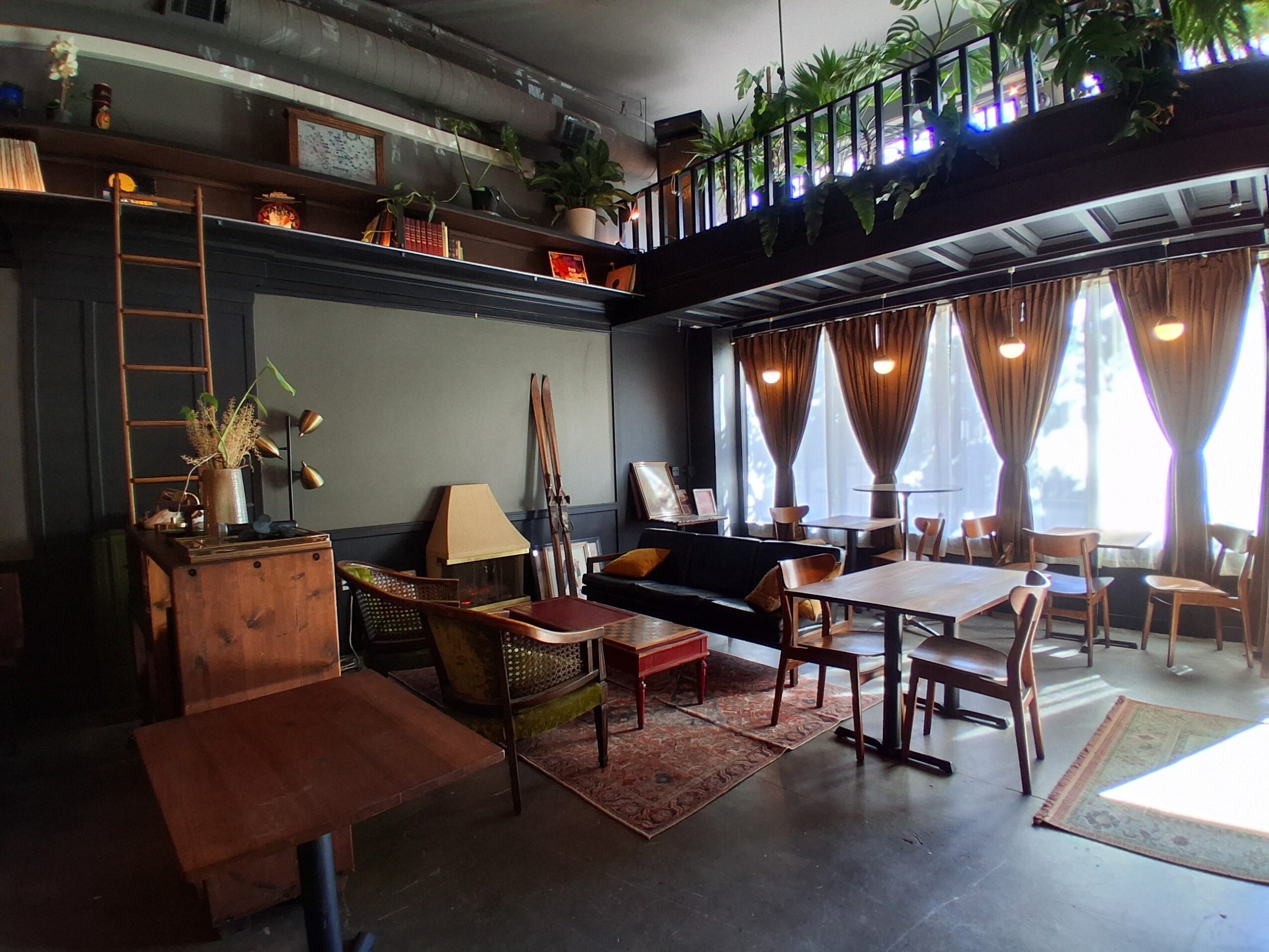 Interior of a cozy room with various chairs, tables, and a window with curtains, decorated with plants and warm lighting.