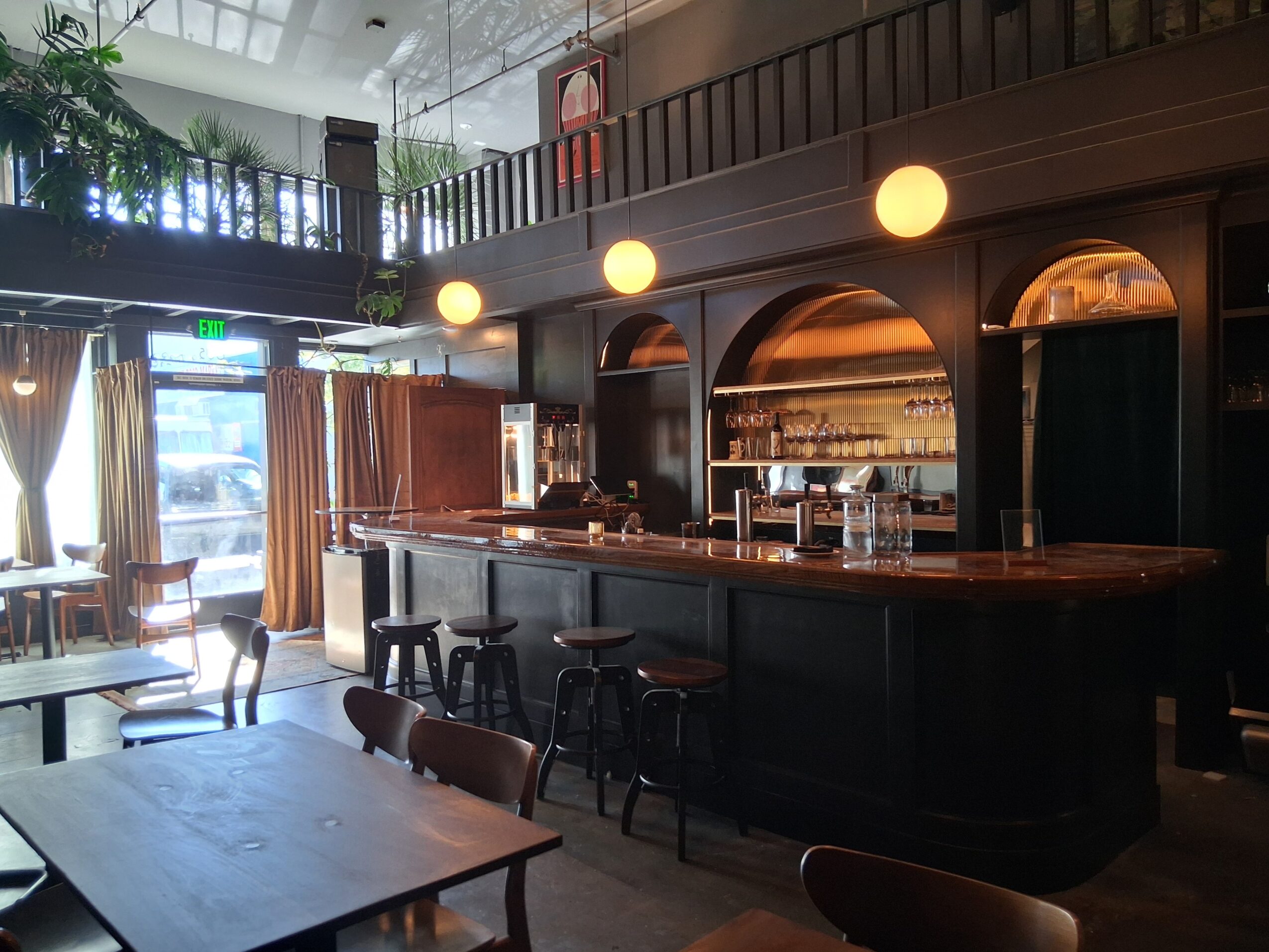 Bar area with a curved counter, shelves with glasses, and warm lighting, in a cozy, dimly lit setting.
