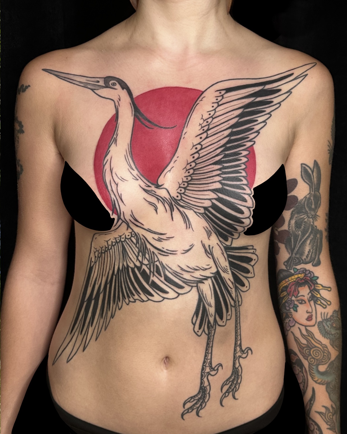 Tattoo of a flying bird with outstretched wings on person's chest, with a red circle background, and tattoos on arms.