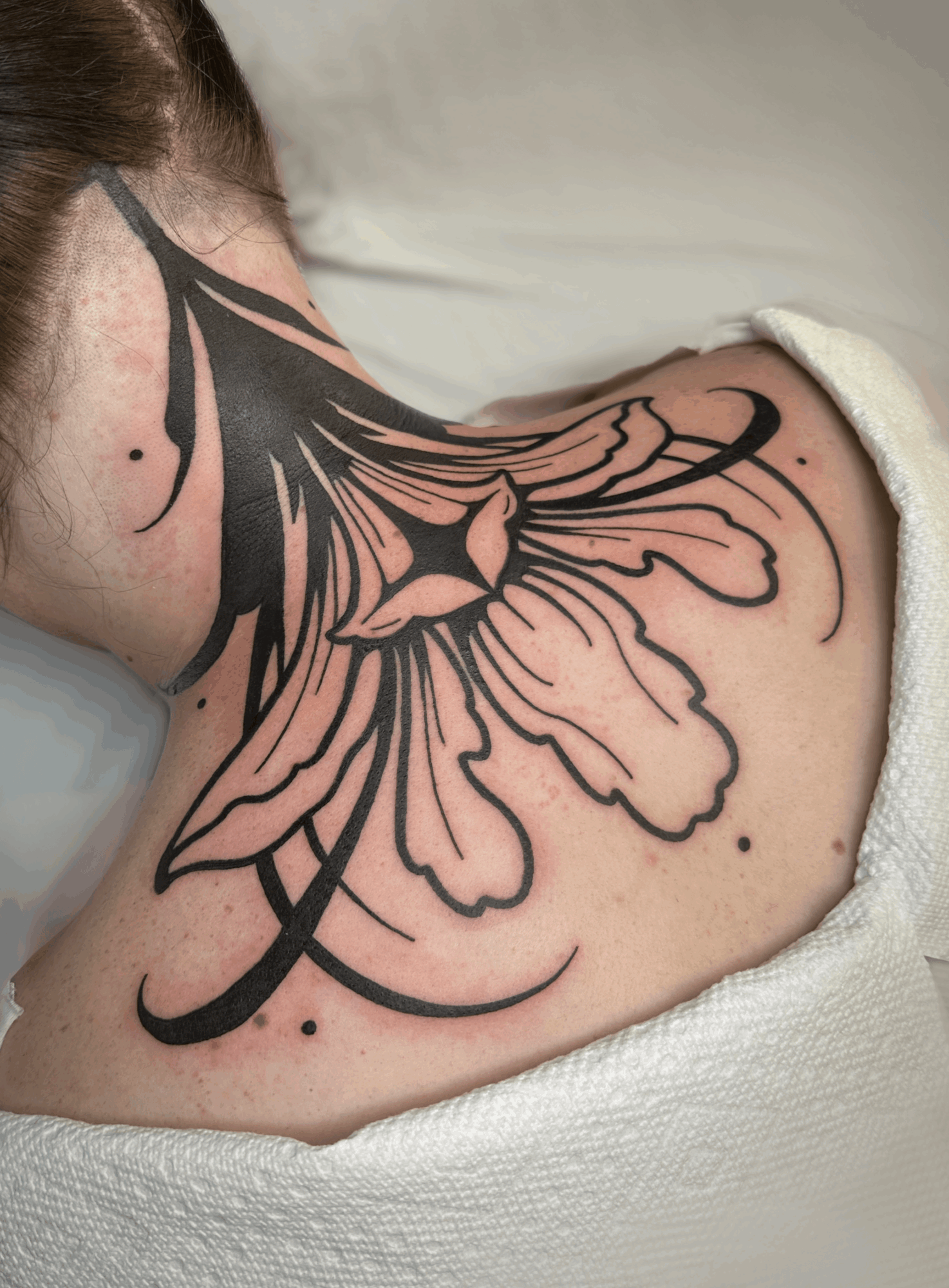 Tattoo of a large, detailed flower on person's shoulder and upper back, with bold black outlines and shading.