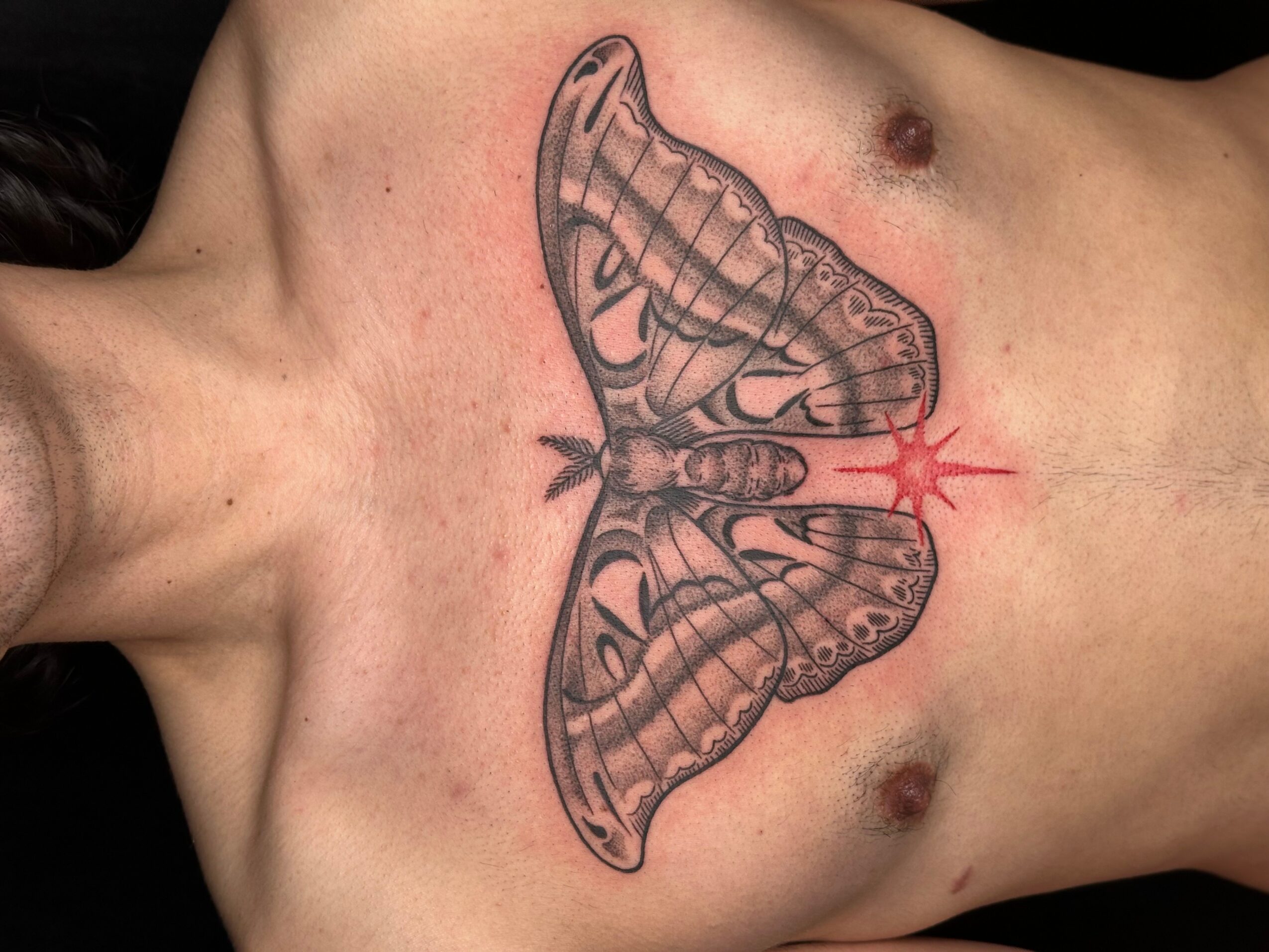 Tattoo of a butterfly with detailed wings on a person's chest, with a red starburst near the center.