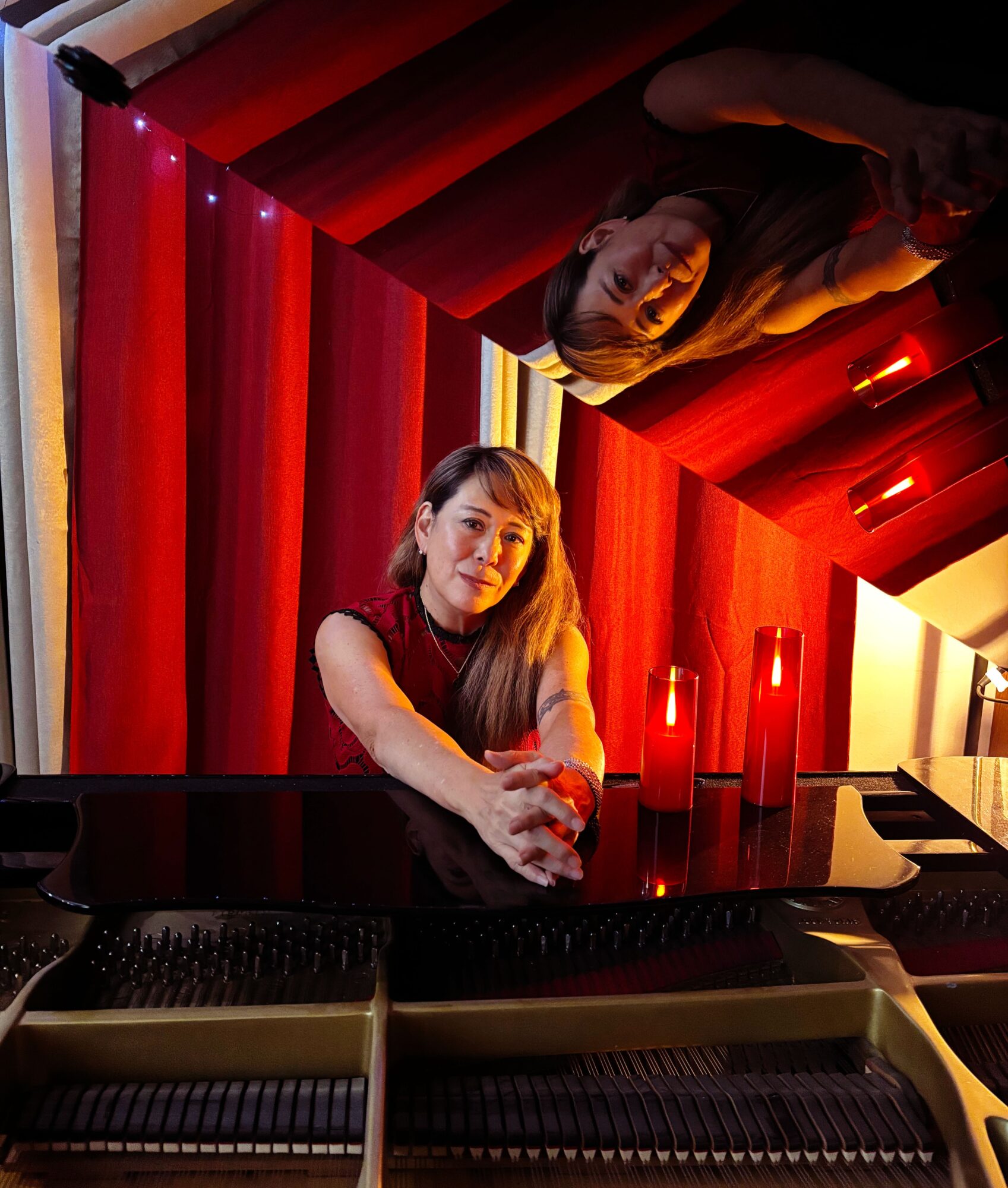 Woman sitting at a piano with red curtains and bottles, reflected in a mirror, in a dimly lit room.