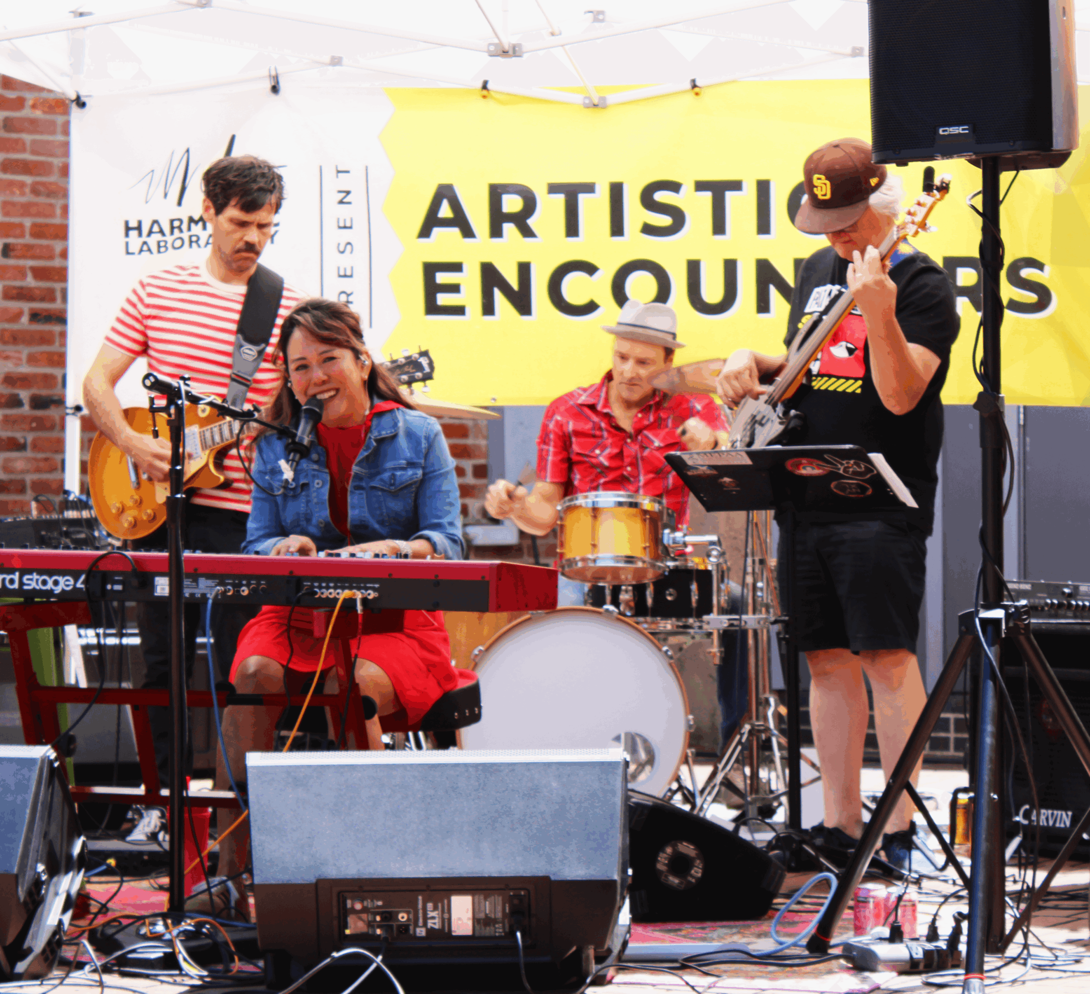 Group of four musicians performing on stage with instruments and a yellow banner reading 'ARTISTIC ENCOUNTERS'.
