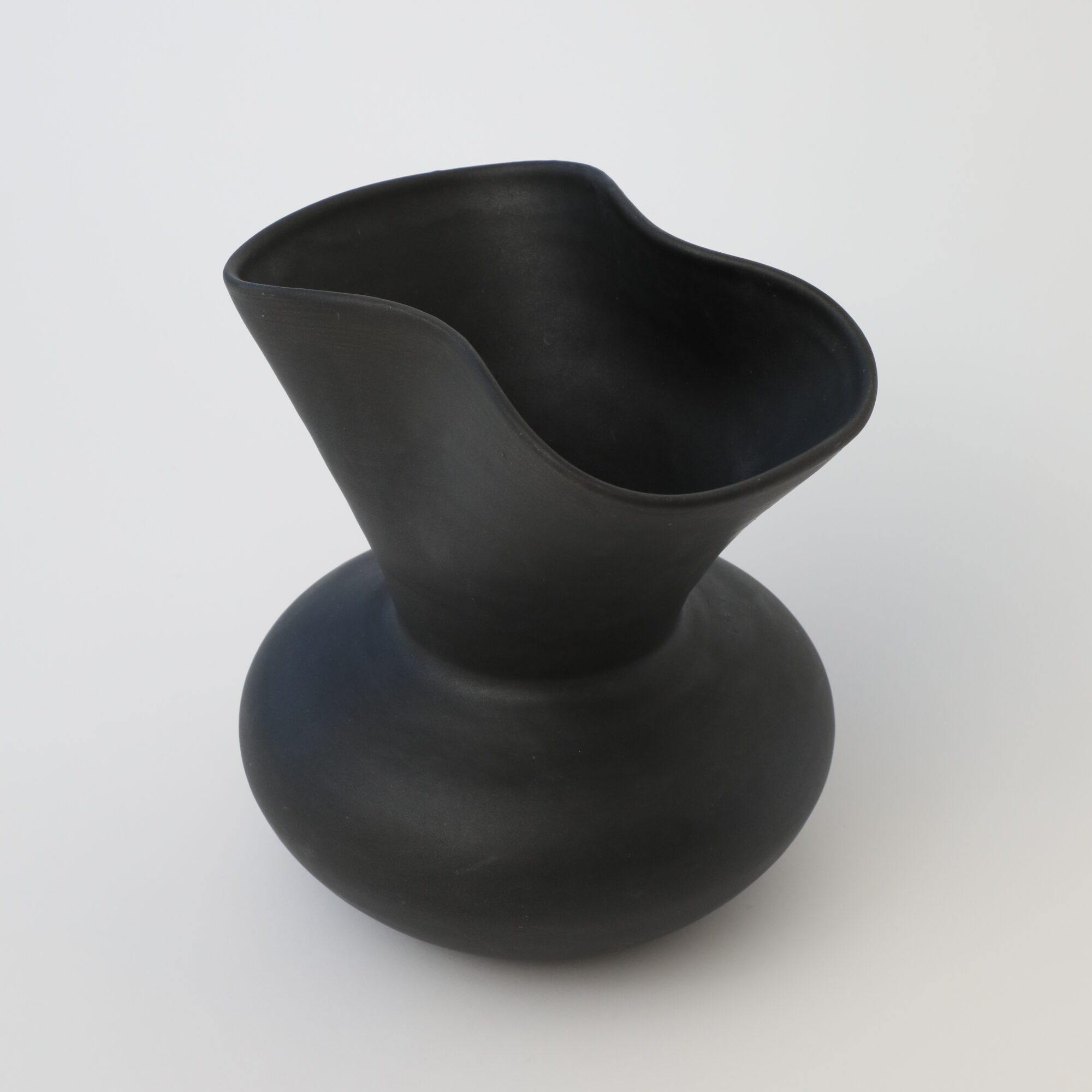 Black vase with a wide, rounded base and a flared, asymmetrical opening, on a white background.