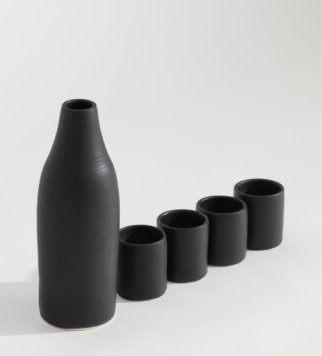 Black vase with four matching cups arranged in a line on a white background.