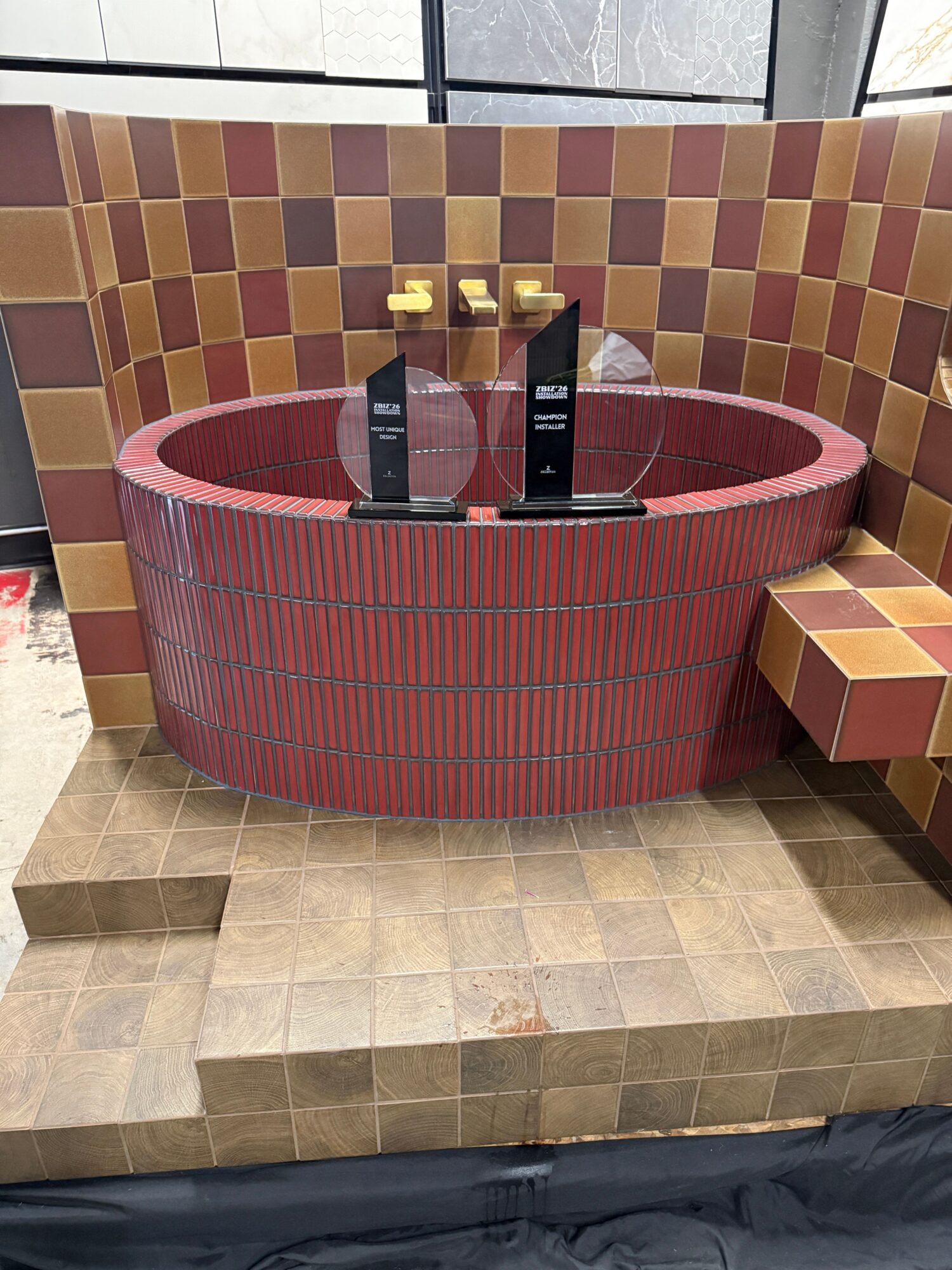 A circular red and brown tiled structure with two black bottles and yellow objects on top, against a checkered wall.