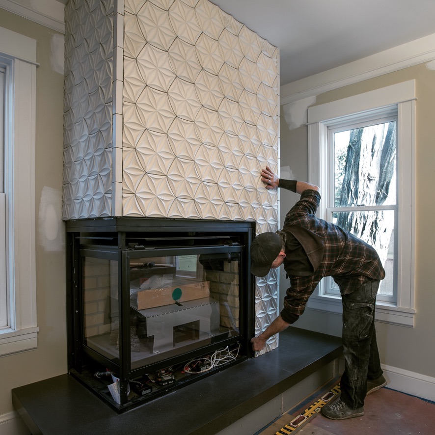 Person adjusting a large, textured, beige fabric cover on a tall structure inside a room with windows and a fireplace.