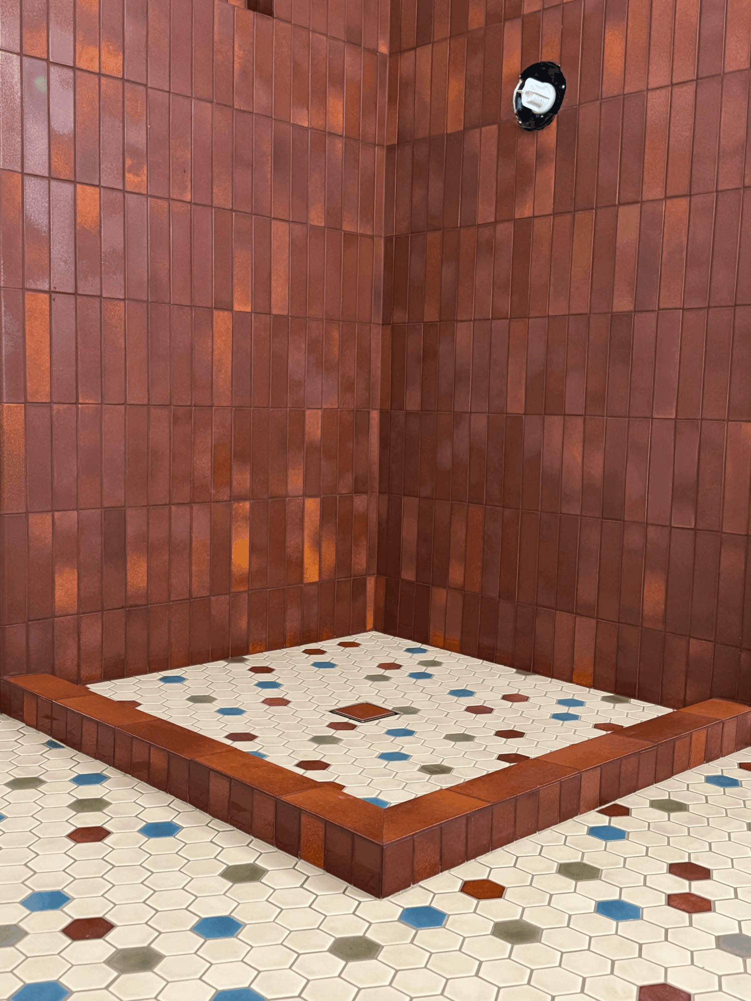 Corner shower area with a tiled wall and a raised platform, with a patterned floor and a showerhead on the wall.