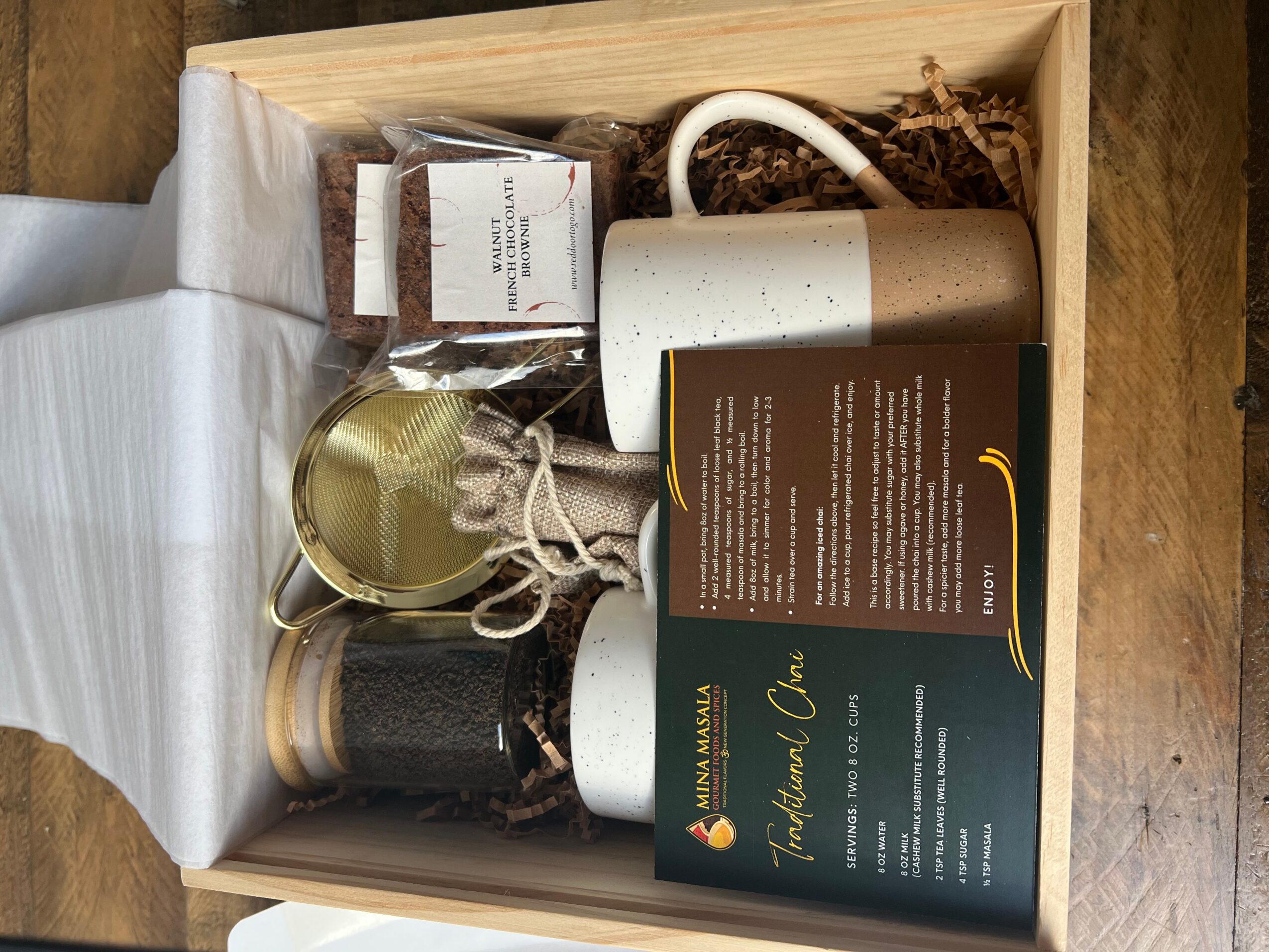 Open box containing tea accessories, a box of tea, a mug, and a spoon, with a wooden surface background.
