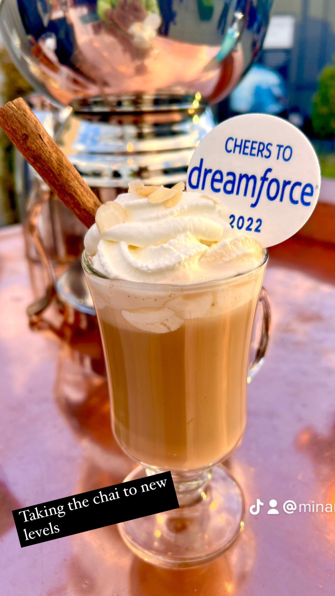 Coffee drink topped with whipped cream, a cookie, and a sign reading 'Cheers to dreamforce 2022', on a table.