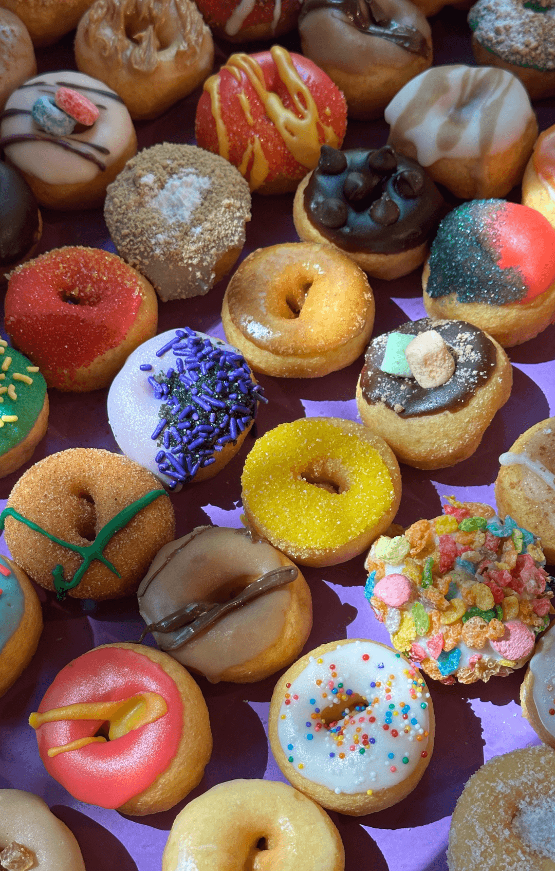 Assorted colorful donuts with various toppings and glazes, arranged closely together.