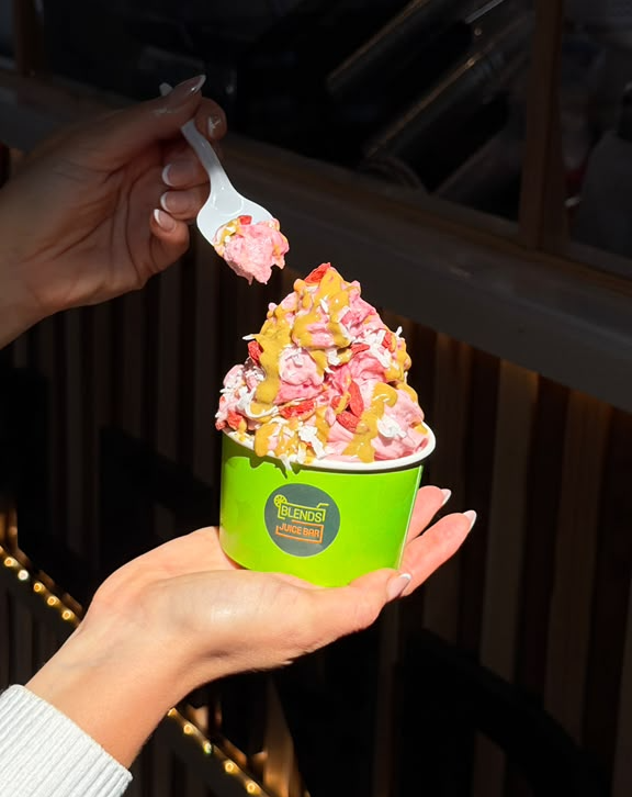 Person holding a cup of colorful ice cream with a white spoon, background of a wooden interior.