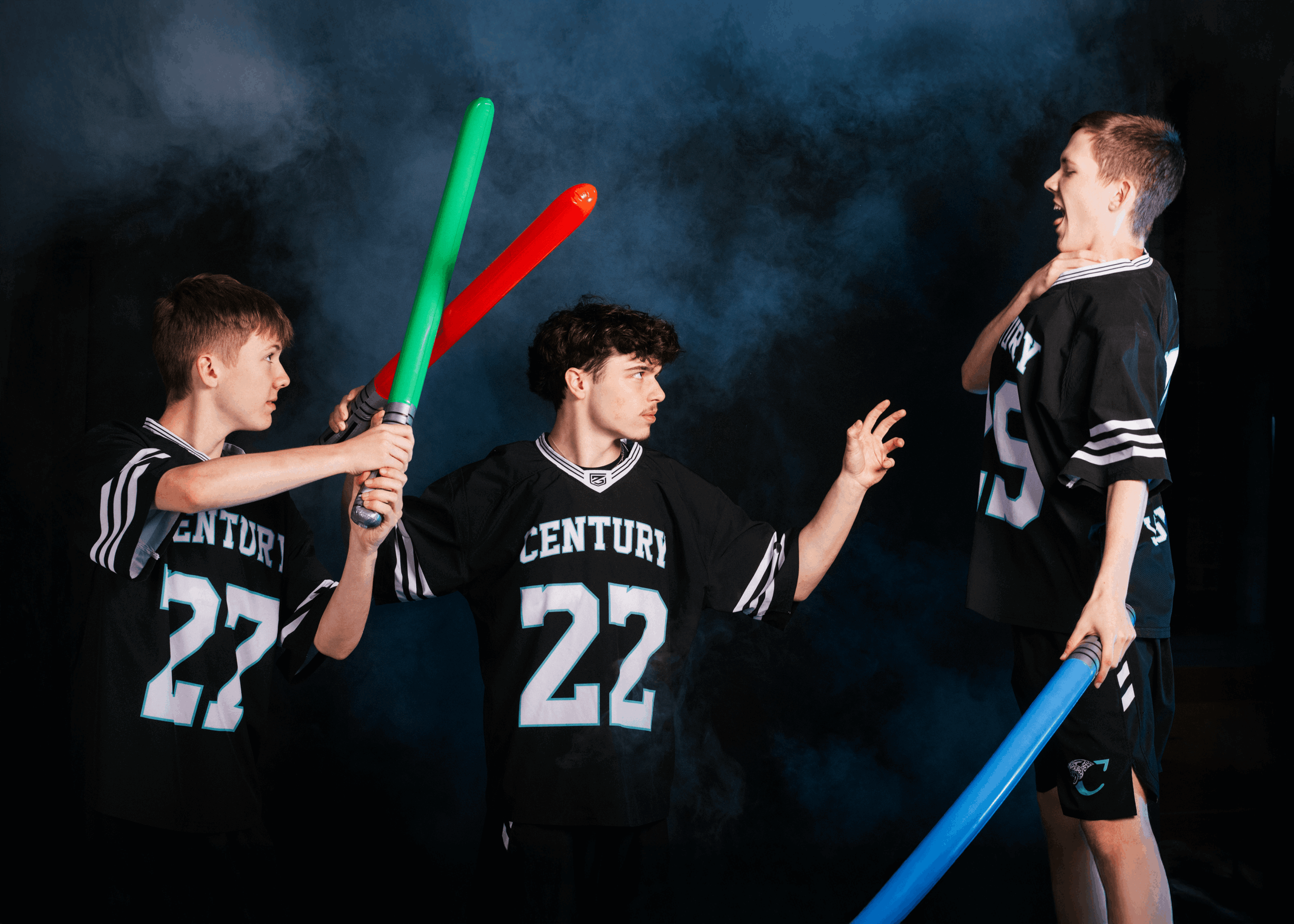 Three boys in sports jerseys holding foam swords, one boy standing with hand on chin, dark background with smoke