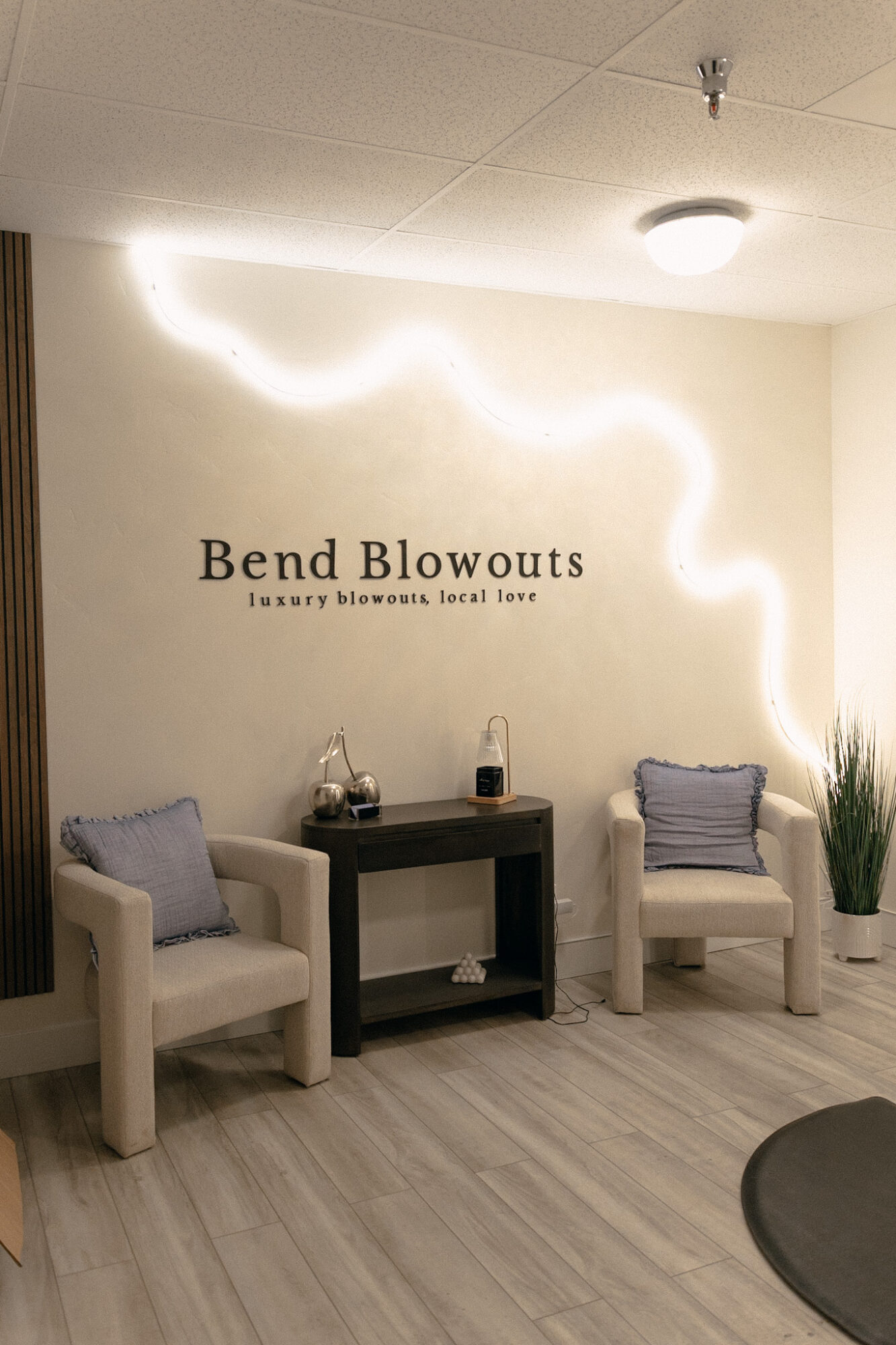 Two white chairs with gray pillows flank a small black table in a room with a wall sign and decorative lighting.