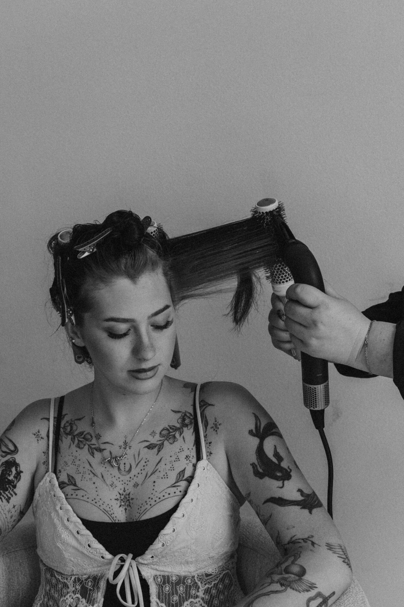 Woman with tattoos getting her hair dried with a hairdryer, eyes closed, in black and white.
