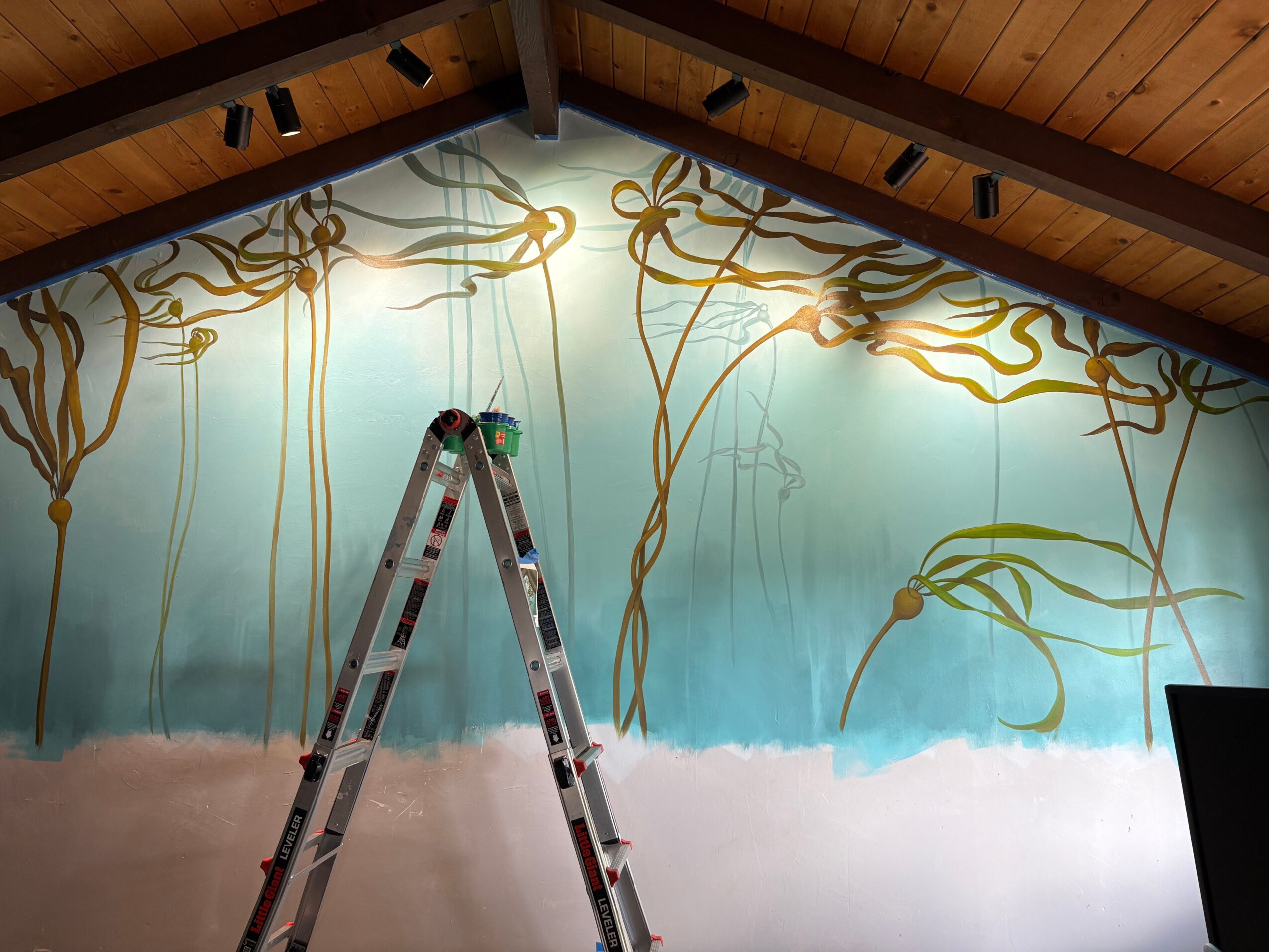 Interior wall with a mural of vines and sky, ladder in front, wooden ceiling above.