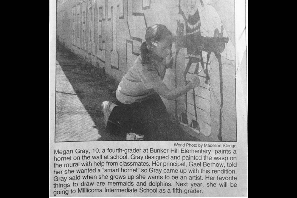 Person crouching and drawing on a wall with geometric patterns, wearing glasses and a striped shirt.