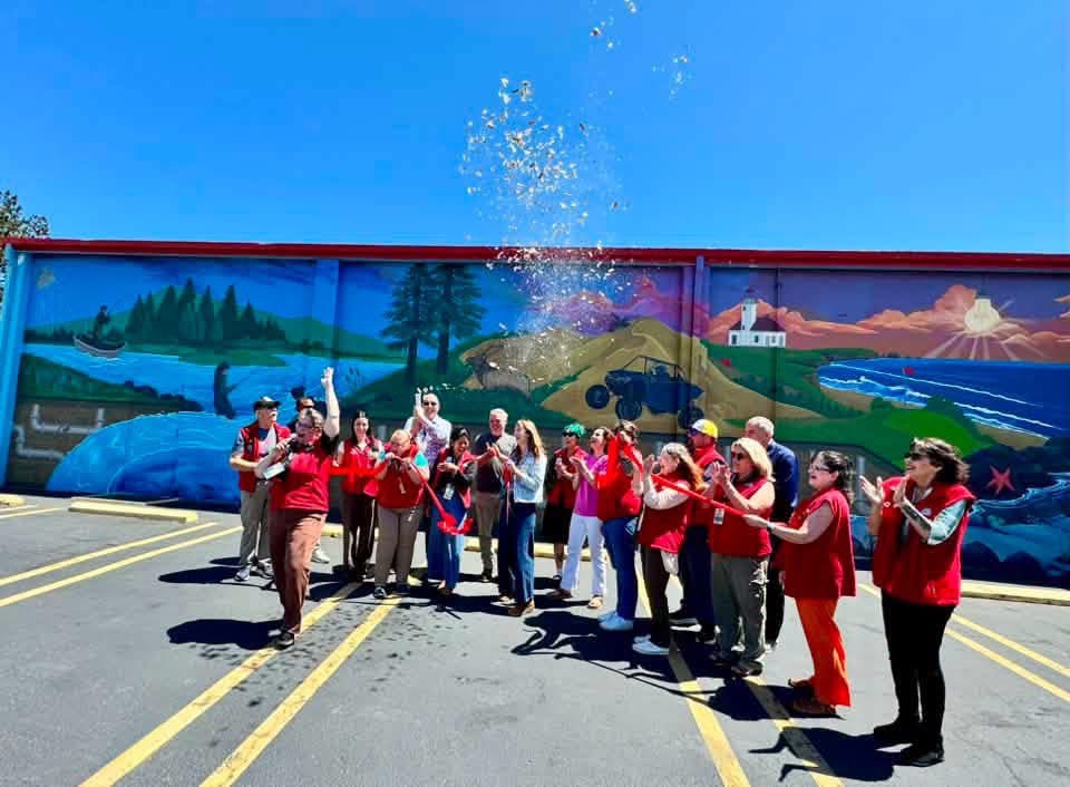 Group of people celebrating outdoors in front of a colorful mural, some wearing red, with a spray of water in the air.