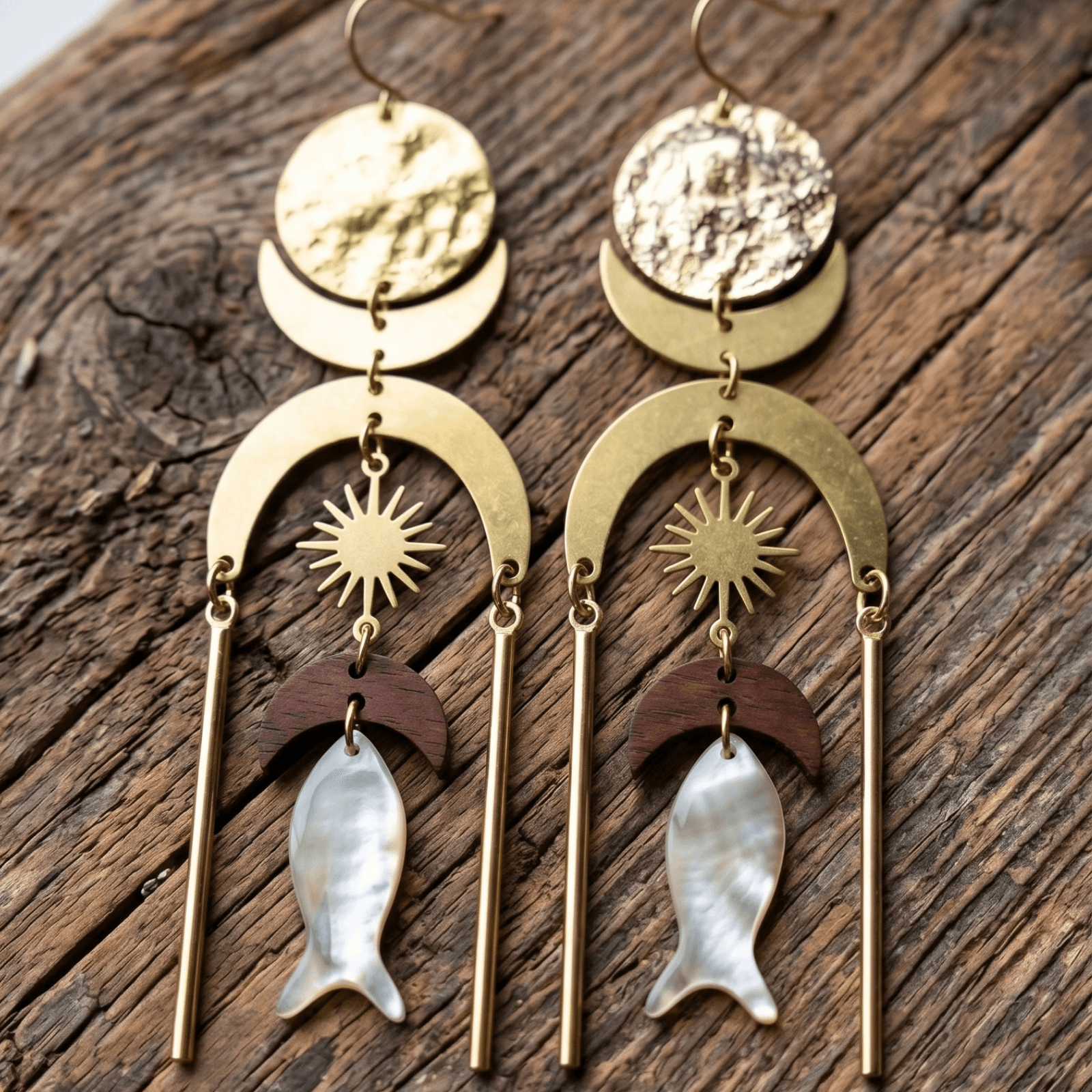 Pair of gold and wood earrings with fish and sun designs on a wooden surface.