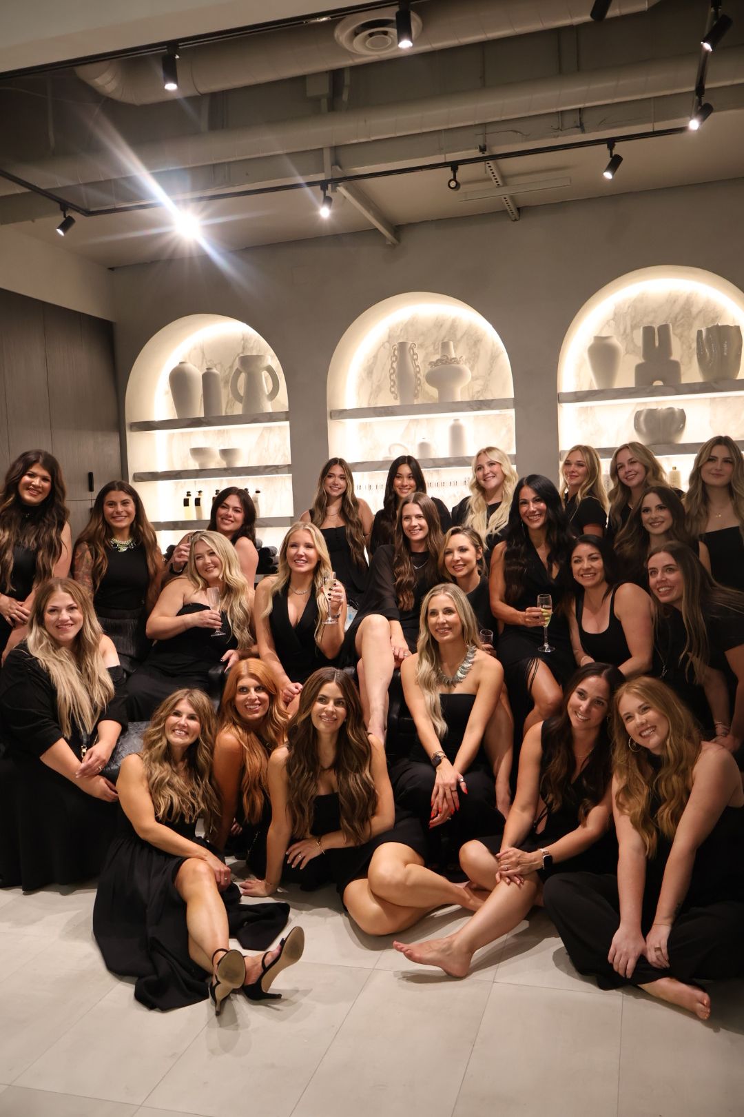 Group of women sitting and standing together in a modern indoor space with illuminated arches, posing for a photo.