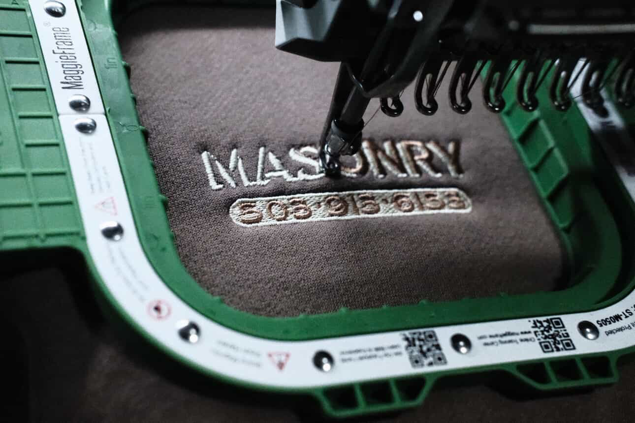 Close-up of a brown mat with the word 'MASONRY' embroidered, surrounded by green and black tools and equipment.