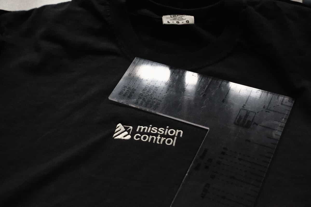 Black shirt with a Mission Control logo and a ruler placed on top, measuring the shirt's width.