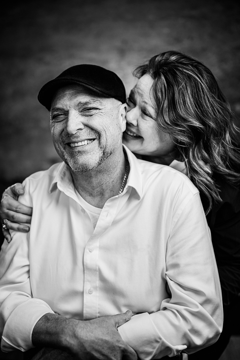 Woman kisses man on the cheek, both smiling, man wearing a hat and white shirt, woman with wavy hair, black and white photo.